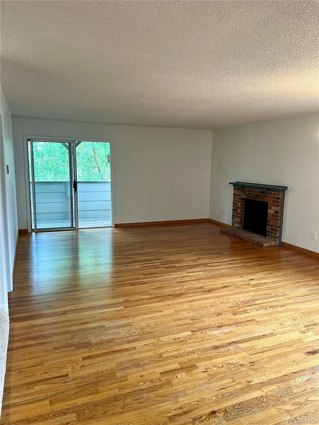 unfurnished living room featuring a textured ceiling, light wood-style flooring, baseboards, and a brick fireplace