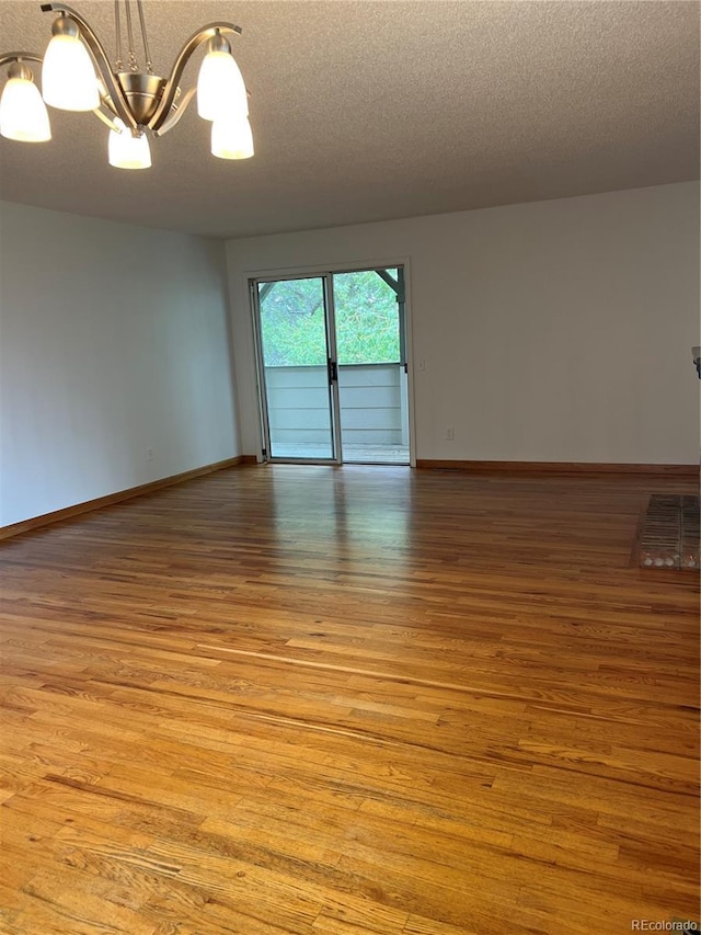 unfurnished room with a chandelier, light wood finished floors, a textured ceiling, and baseboards
