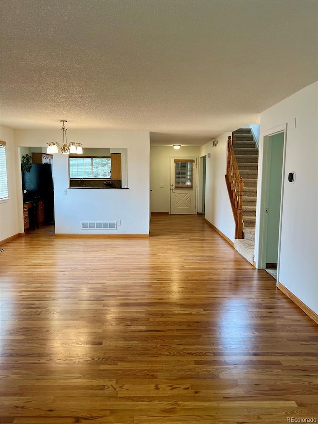 unfurnished living room featuring a chandelier, wood finished floors, stairs, and a textured ceiling