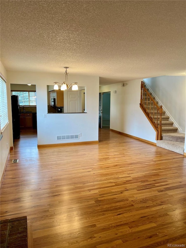 unfurnished living room with a textured ceiling, a chandelier, light wood-style floors, stairs, and baseboards