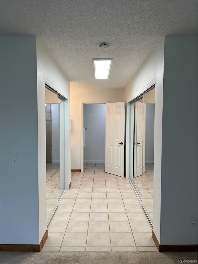 hall with a textured ceiling, baseboards, and light tile patterned flooring