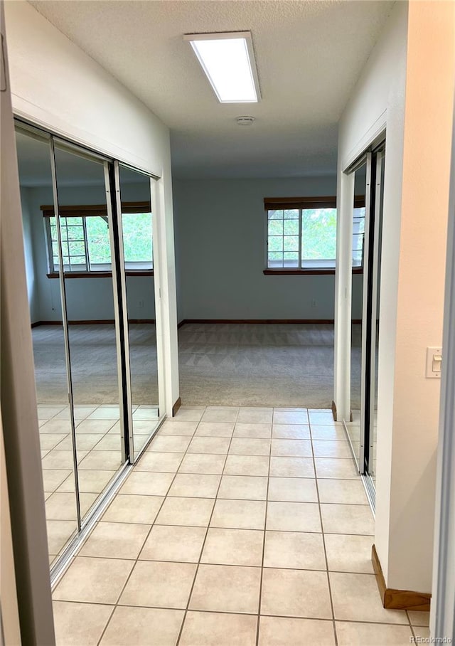 hall with baseboards, light tile patterned flooring, and light carpet