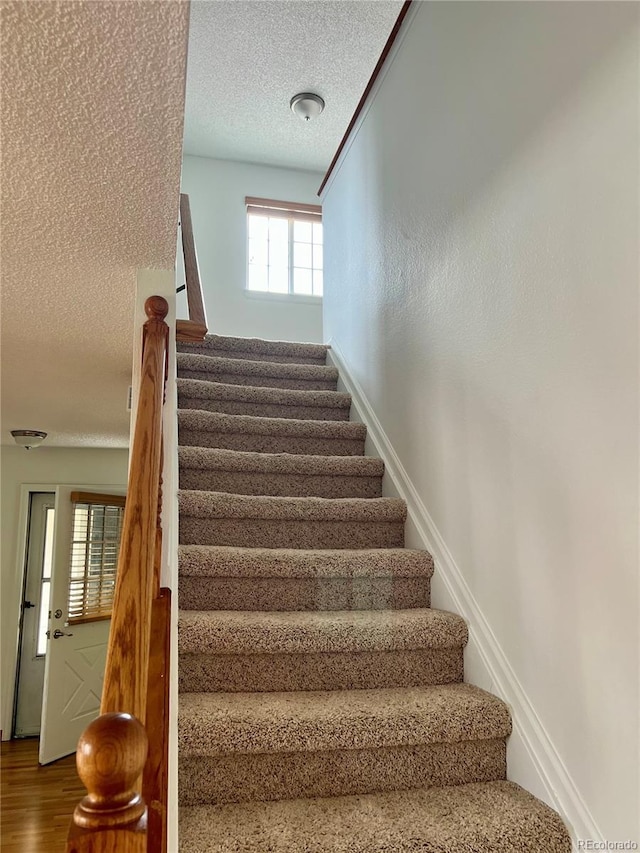 stairway featuring a textured ceiling, wood finished floors, and baseboards