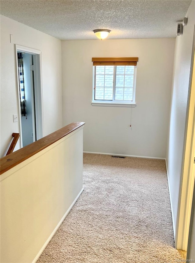 corridor with carpet floors, a textured ceiling, an upstairs landing, and baseboards
