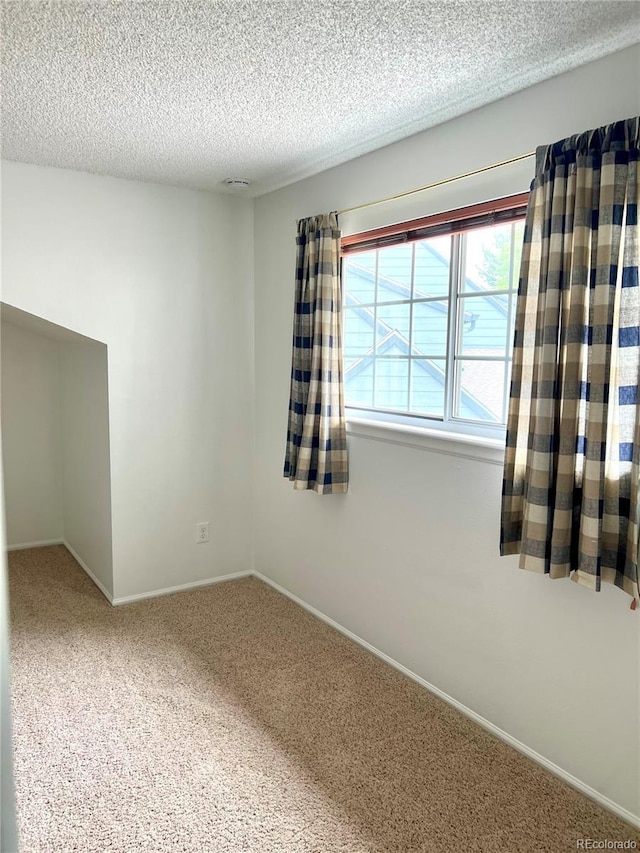 carpeted empty room with a textured ceiling and baseboards