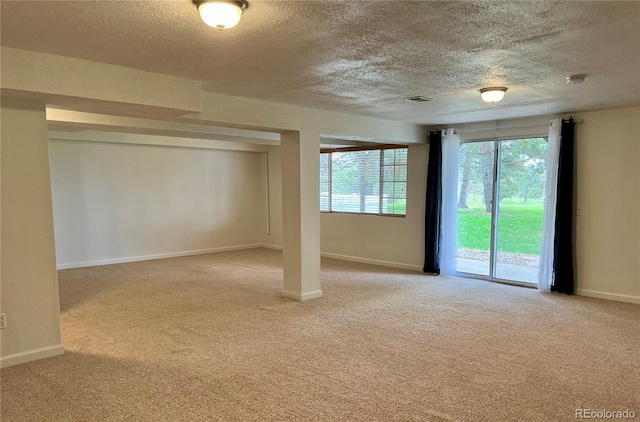 empty room with a textured ceiling, light colored carpet, plenty of natural light, and baseboards