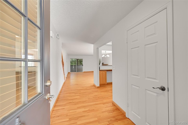 10369 E Red Mtn, Littleton, CO 80127 - hall with light wood-type flooring, baseboards, a textured ceiling, and a chandelier