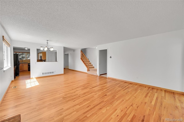 10369 E Red Mtn, Littleton, CO 80127 - unfurnished living room featuring a textured ceiling, a chandelier, light wood-style flooring, stairway, and baseboards