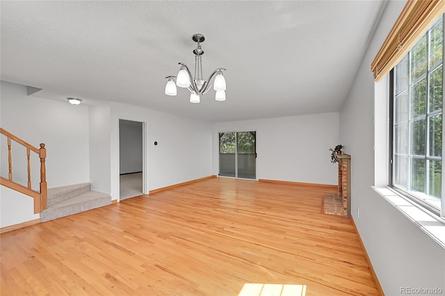 10369 E Red Mtn, Littleton, CO 80127 - unfurnished room featuring light wood-style flooring, stairs, a chandelier, baseboards, and a textured ceiling