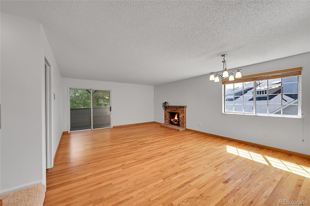 10369 E Red Mtn, Littleton, CO 80127 - unfurnished living room featuring light wood-style floors, a chandelier, a textured ceiling, baseboards, and a brick fireplace