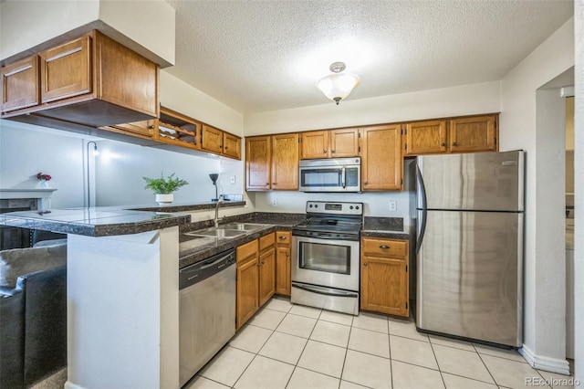 kitchen featuring appliances with stainless steel finishes, a sink, brown cabinetry, a peninsula, and a textured ceiling