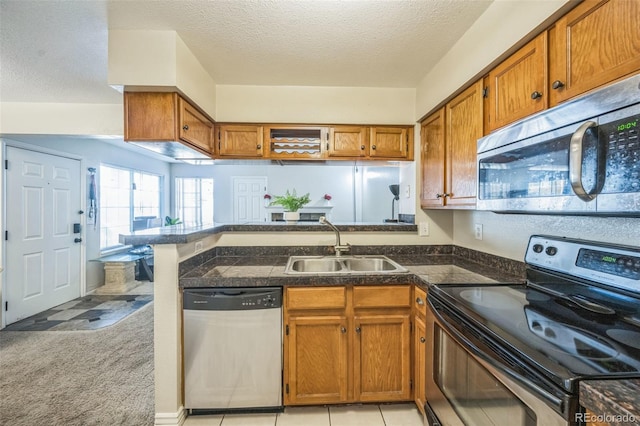 kitchen with stainless steel appliances, a sink, a peninsula, brown cabinets, and a textured ceiling