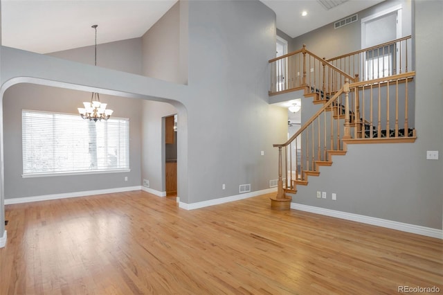 unfurnished living room featuring hardwood / wood-style flooring, high vaulted ceiling, and an inviting chandelier