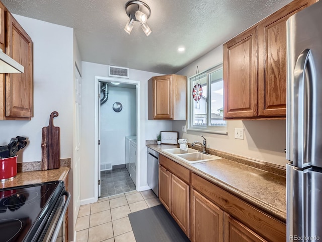 kitchen featuring sink, stainless steel appliances, a textured ceiling, light tile patterned floors, and washer and dryer