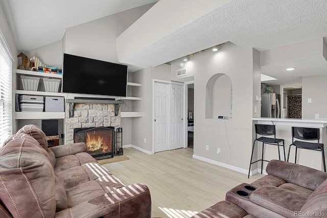 living area with a textured ceiling, visible vents, wood finished floors, and a stone fireplace