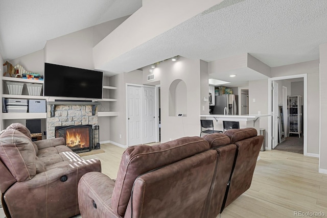 living room with light wood finished floors, baseboards, visible vents, a textured ceiling, and a fireplace