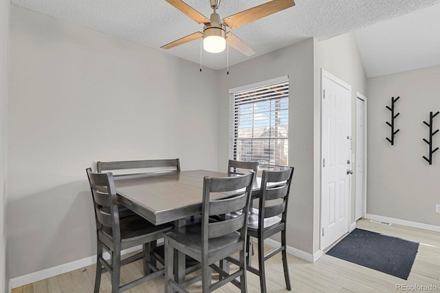 dining space featuring a textured ceiling, light wood finished floors, and baseboards