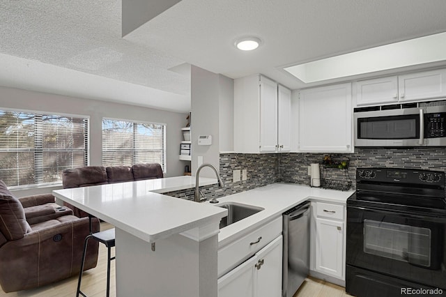 kitchen featuring open floor plan, a peninsula, light countertops, stainless steel appliances, and a sink