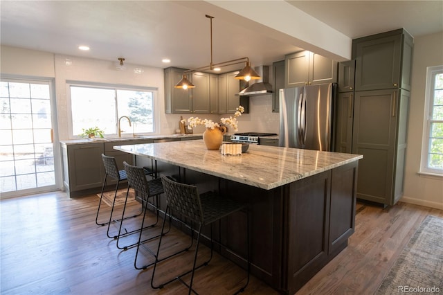 7600 S Ulster Ct, Centennial, CO 80112 - kitchen featuring freestanding refrigerator, wall chimney exhaust hood, a sink, a kitchen island, and light stone counters