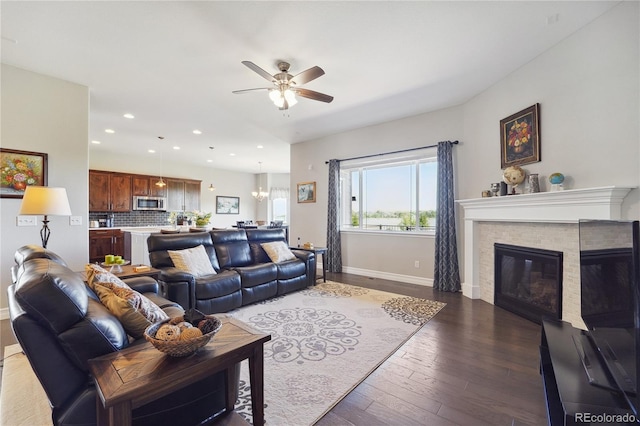 living room featuring ceiling fan with notable chandelier, a fireplace, and dark hardwood / wood-style floors