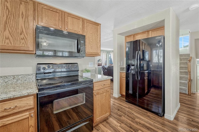 kitchen with light stone countertops, a textured ceiling, light hardwood / wood-style flooring, and black appliances