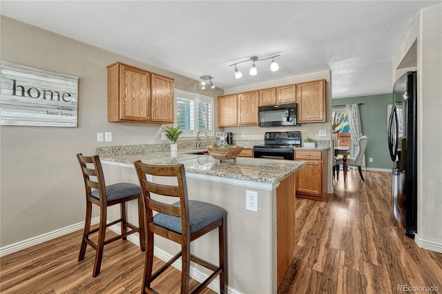 kitchen with a breakfast bar, light stone counters, kitchen peninsula, hardwood / wood-style flooring, and black appliances