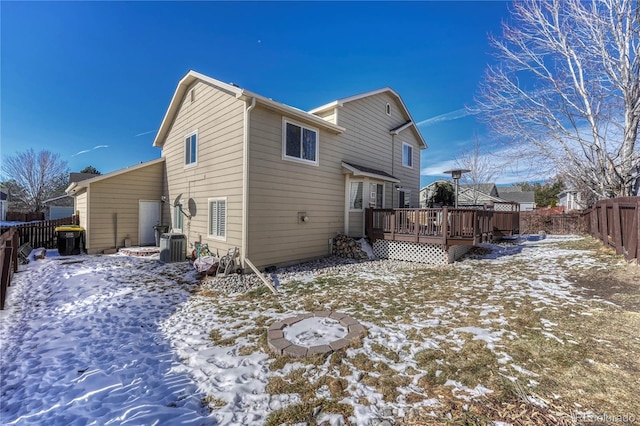 snow covered house with a wooden deck, central AC unit, and an outdoor fire pit