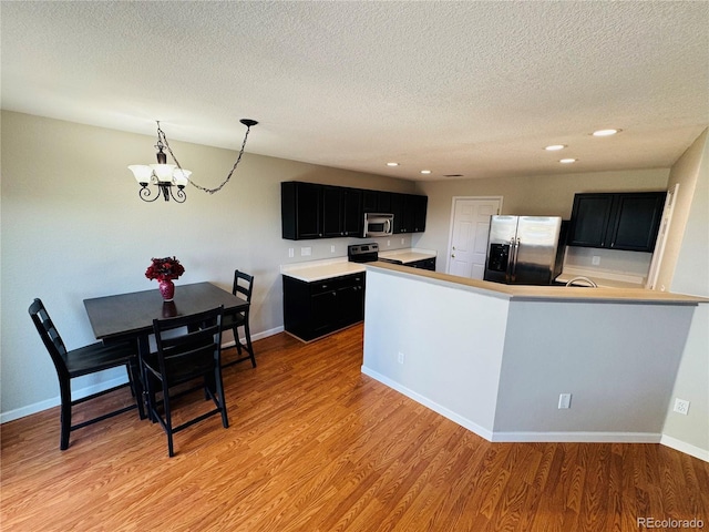 kitchen with pendant lighting, light hardwood / wood-style floors, kitchen peninsula, stainless steel appliances, and a textured ceiling