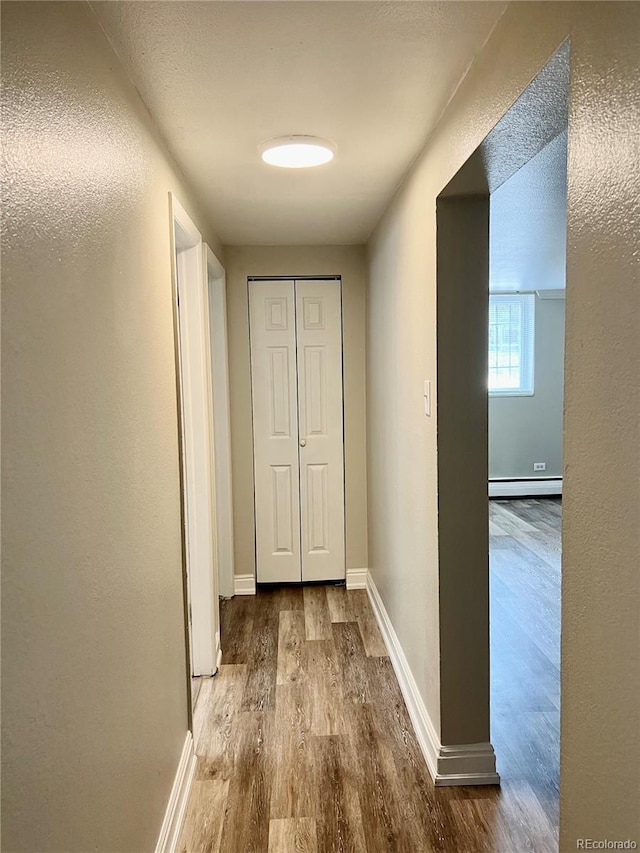 corridor featuring baseboards, wood finished floors, and baseboard heating