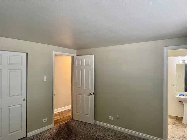 unfurnished bedroom featuring connected bathroom, a textured ceiling, and baseboards
