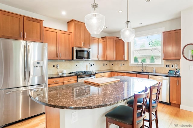 4414 Wolff St, Denver, CO 80212 - kitchen featuring stainless steel appliances, light wood finished floors, a kitchen island, a breakfast bar area, and dark stone counters