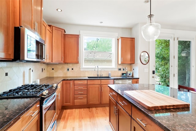 4414 Wolff St, Denver, CO 80212 - kitchen featuring appliances with stainless steel finishes, light wood-style flooring, dark stone counters, hanging light fixtures, and brown cabinetry
