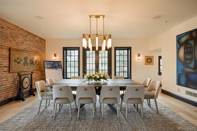 dining space featuring visible vents, light wood-style flooring, brick wall, and a healthy amount of sunlight