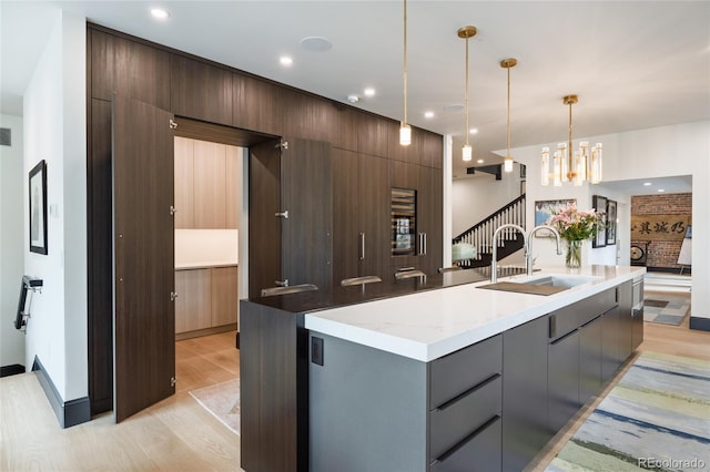 kitchen featuring a sink, light wood-style flooring, decorative light fixtures, a spacious island, and modern cabinets