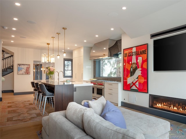 living area with recessed lighting, light wood finished floors, a glass covered fireplace, and stairway