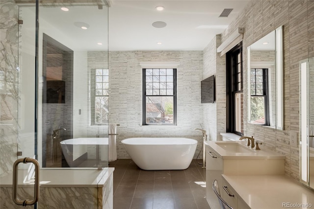 bathroom with visible vents, tile walls, vanity, tile patterned floors, and a soaking tub