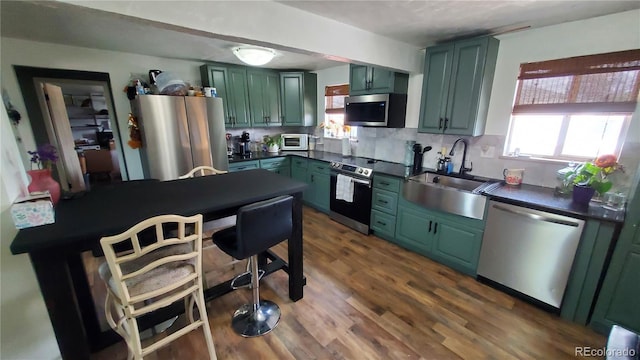 kitchen with a sink, green cabinetry, appliances with stainless steel finishes, and dark countertops
