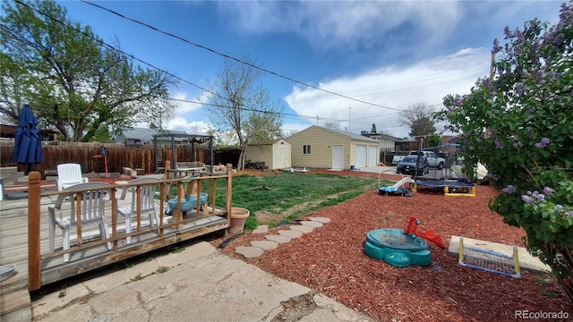 view of yard with a trampoline, an outbuilding, a garage, fence, and a storage unit