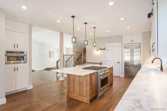 kitchen featuring a center island, sink, premium appliances, light stone counters, and white cabinets