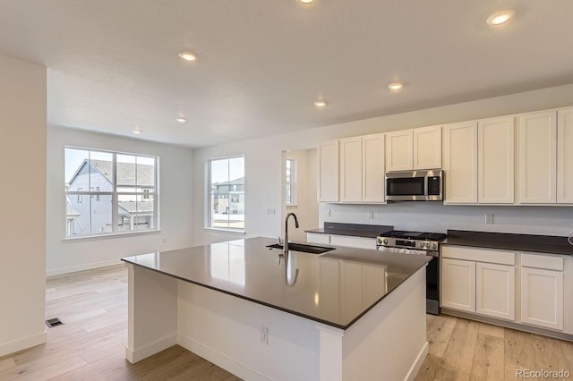 kitchen with stainless steel appliances, light wood-type flooring, dark countertops, and a sink