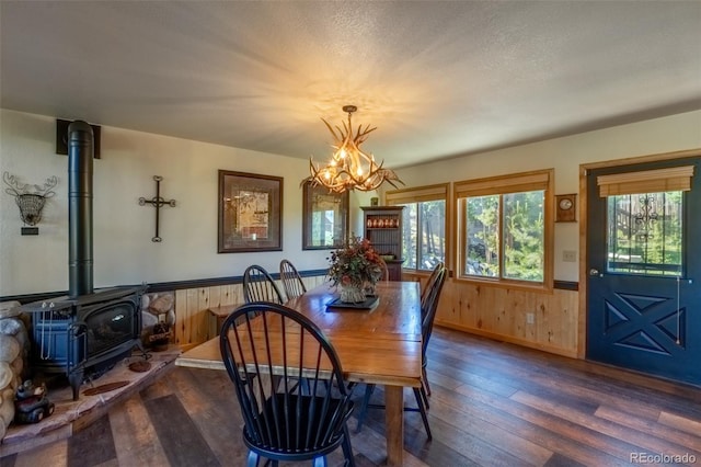 dining space with dark hardwood / wood-style floors, wood walls, a wood stove, and a chandelier