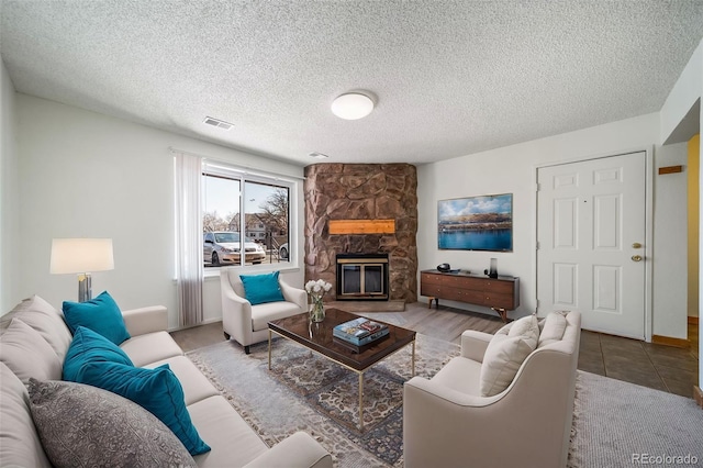 living room with a textured ceiling, visible vents, and a stone fireplace