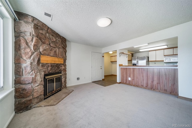 unfurnished living room with a textured ceiling, baseboards, a stone fireplace, visible vents, and light carpet