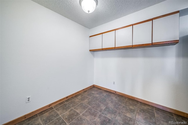 spare room featuring a textured ceiling and baseboards