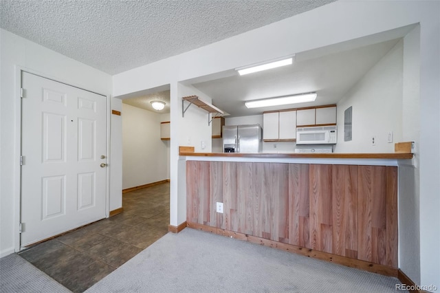 kitchen featuring a peninsula, dark tile patterned floors, stainless steel fridge, baseboards, and white microwave