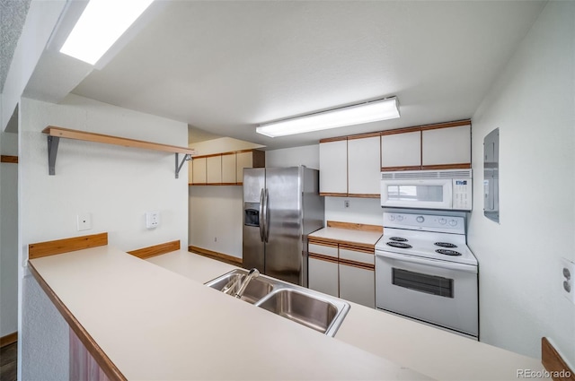 kitchen featuring a sink, a peninsula, white appliances, and light countertops