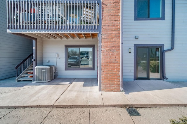 doorway to property with a balcony, cooling unit, a patio area, and brick siding