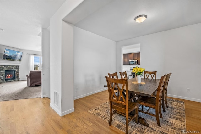 dining room with light wood-style floors, baseboards, a fireplace, and visible vents