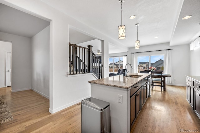 kitchen with pendant lighting, light wood-style floors, a sink, light stone countertops, and baseboards