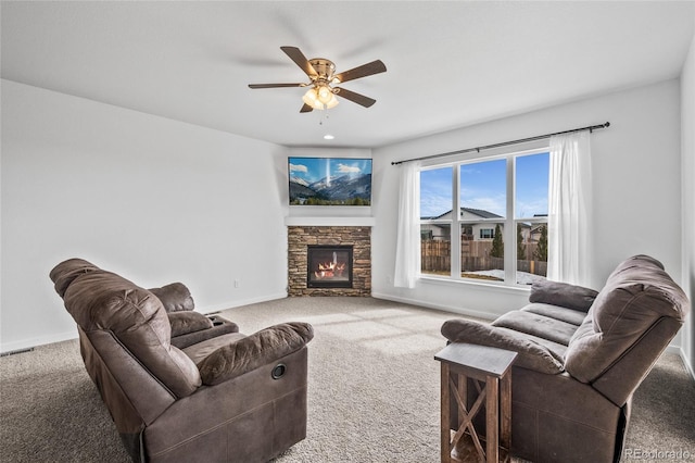 living area featuring carpet floors, a stone fireplace, a ceiling fan, and baseboards